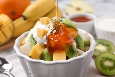 Photo of Pouring honey onto delicious fruit salad in bowl on table, closeup