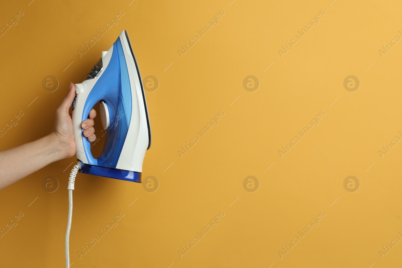 Photo of Woman holding modern iron on orange background, closeup. Space for text