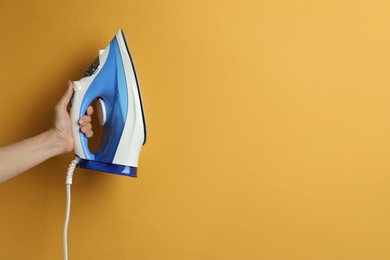 Photo of Woman holding modern iron on orange background, closeup. Space for text