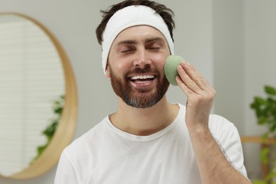 Photo of Man with headband washing his face using sponge in bathroom