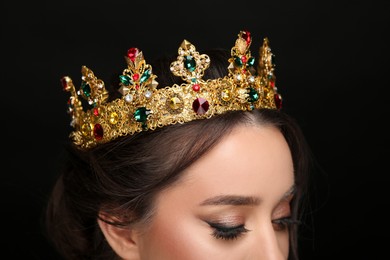 Beautiful young woman wearing luxurious crown on black background, closeup