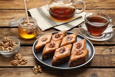 Photo of Delicious sweet baklava with walnuts, honey and hot tea on wooden table