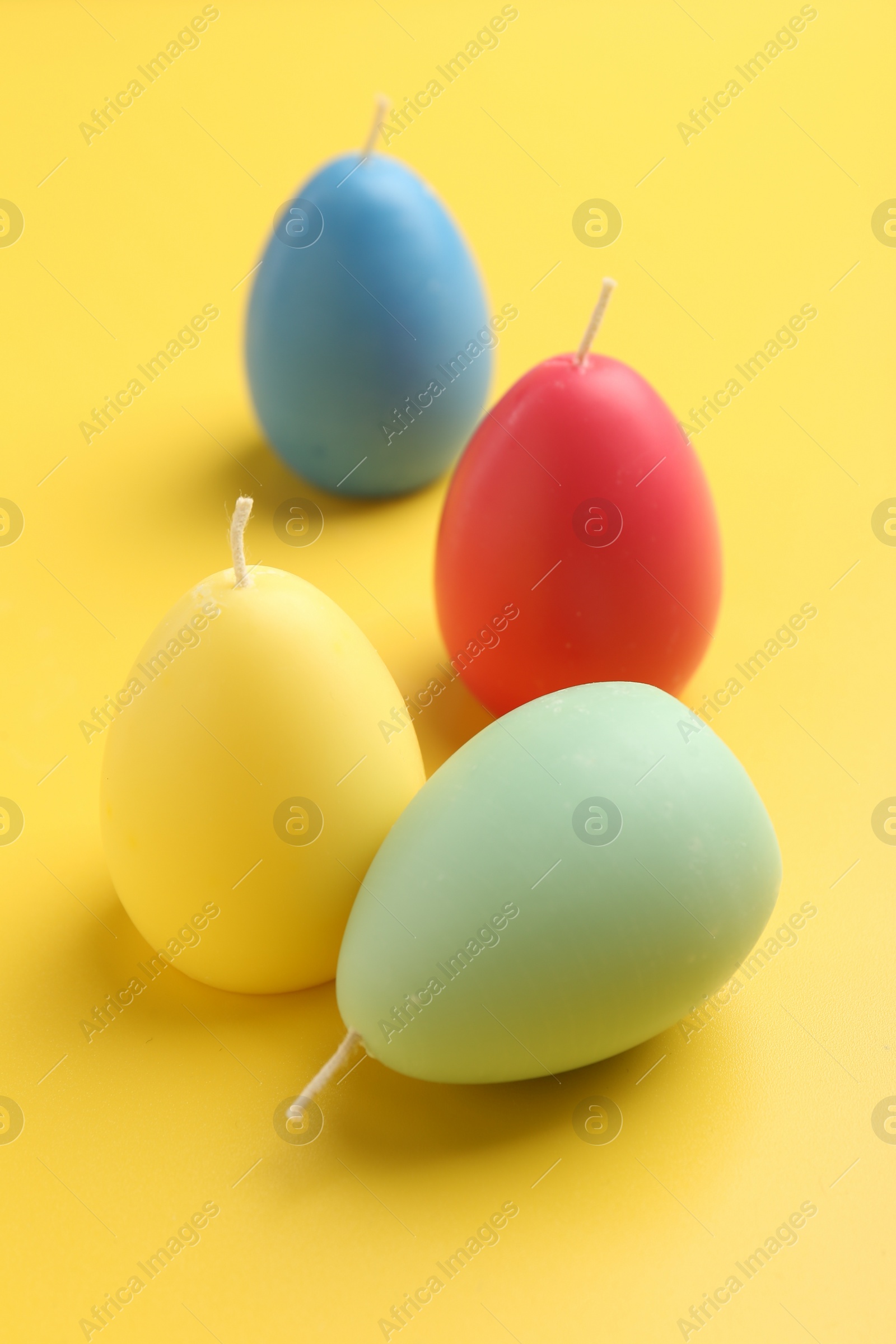 Photo of Colorful egg shaped candles on yellow background. Easter decor