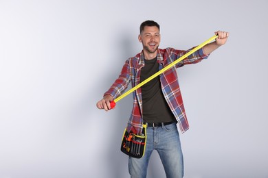 Handsome worker with measuring tape on white background, space for text