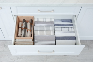 Photo of Open drawer with folded napkins and towels indoors. Order in kitchen
