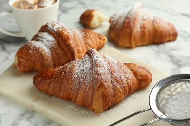 Photo of Tasty croissants with powdered sugar on white marble table, closeup