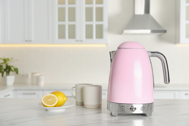 Photo of Modern electric kettle, cups and lemons on table in kitchen