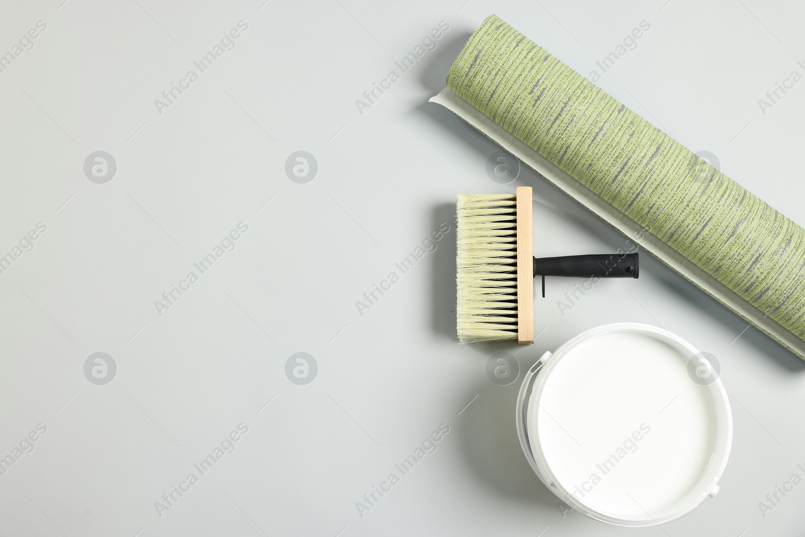 Image of Wallpaper roll, brush and bucket of glue on light grey background, flat lay