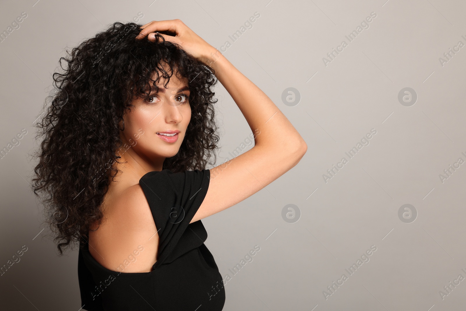 Photo of Beautiful young woman with long curly hair on light grey background. Space for text