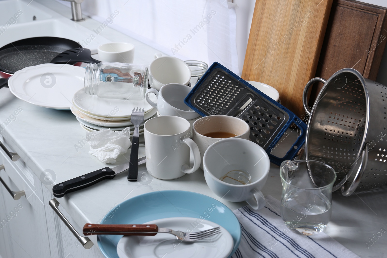 Photo of Many dirty utensils and dishware on countertop in messy kitchen