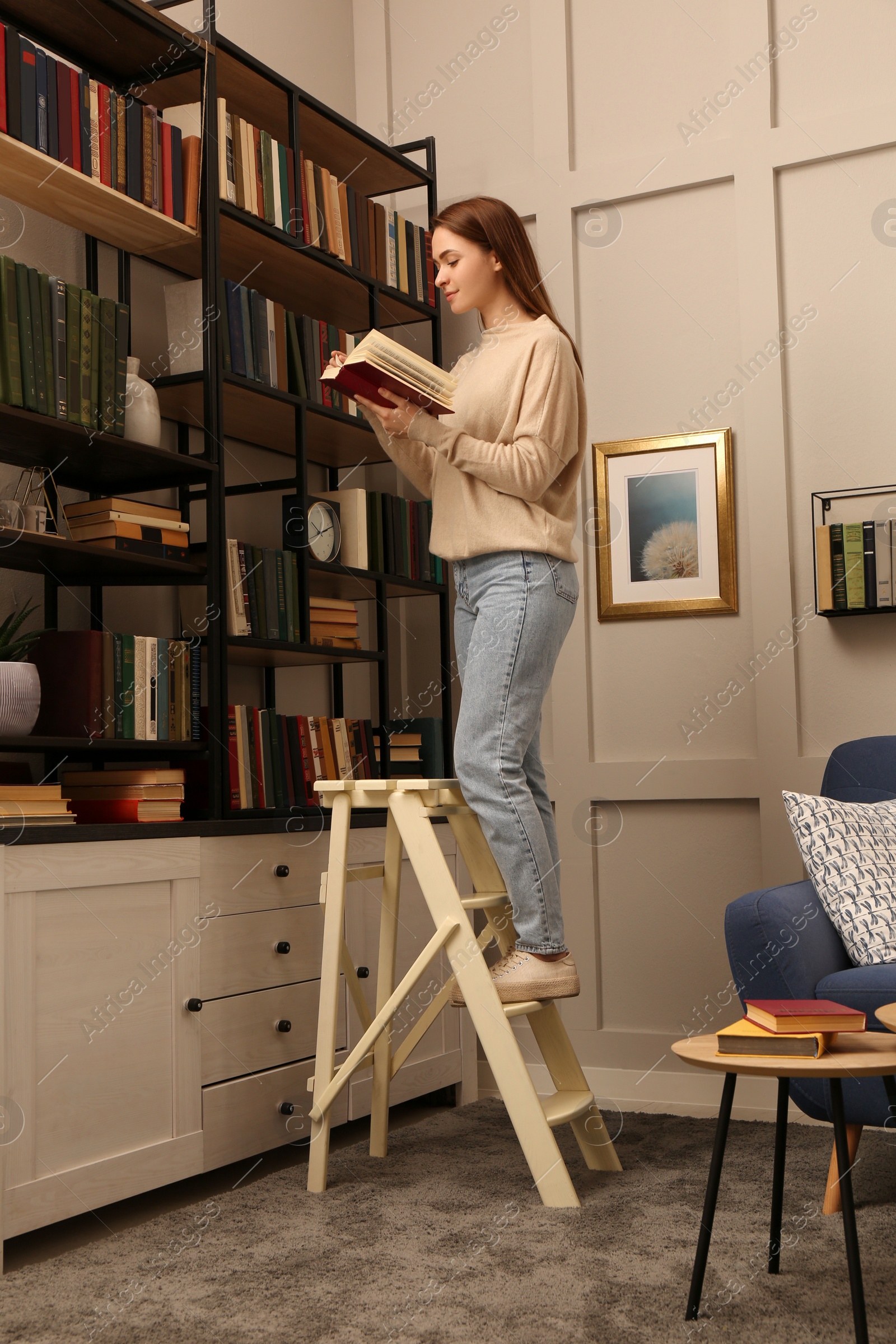 Photo of Young woman choosing book in home library