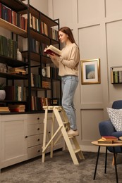 Photo of Young woman choosing book in home library
