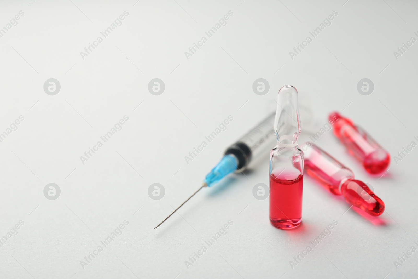 Photo of Glass ampoules with liquid and syringe on white background, closeup. Space for text