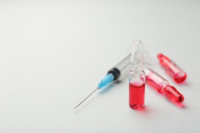 Glass ampoules with liquid and syringe on white background, closeup. Space for text