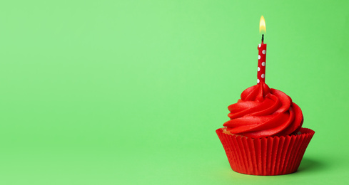 Delicious birthday cupcake with red cream and burning candle on green background. Space for text