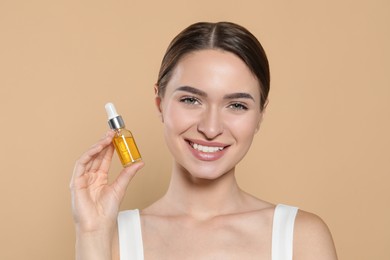 Young woman with bottle of essential oil on beige background