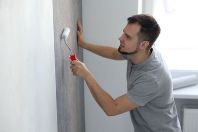 Photo of Man hanging stylish gray wallpaper in room