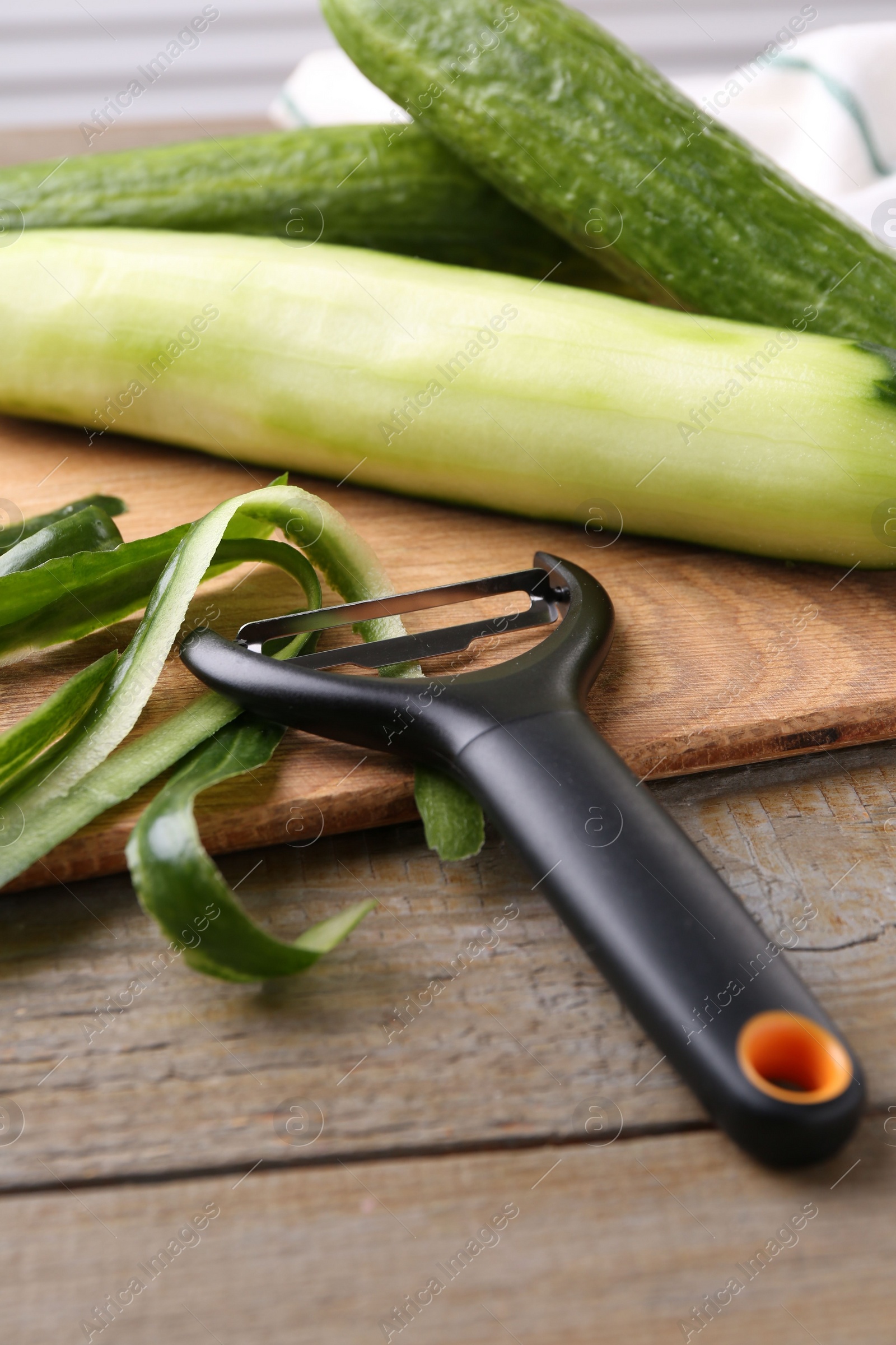 Photo of Fresh cucumbers, peels and peeler at wooden table
