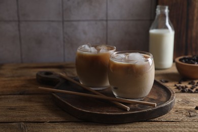 Photo of Refreshing iced coffee with milk in glasses and straws on wooden table