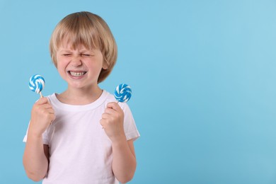 Photo of Emotional little boy with bright lollipops on light blue background, space for text