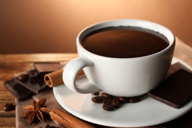 Cup of delicious hot chocolate, spices and coffee beans on wooden table, closeup