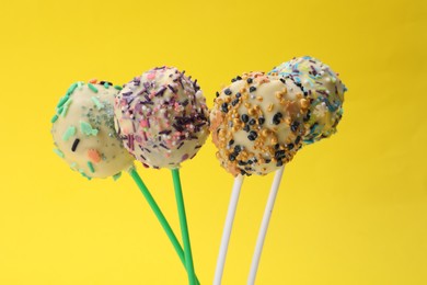 Sweet cake pops decorated with sprinkles on yellow background, closeup. Delicious confectionery