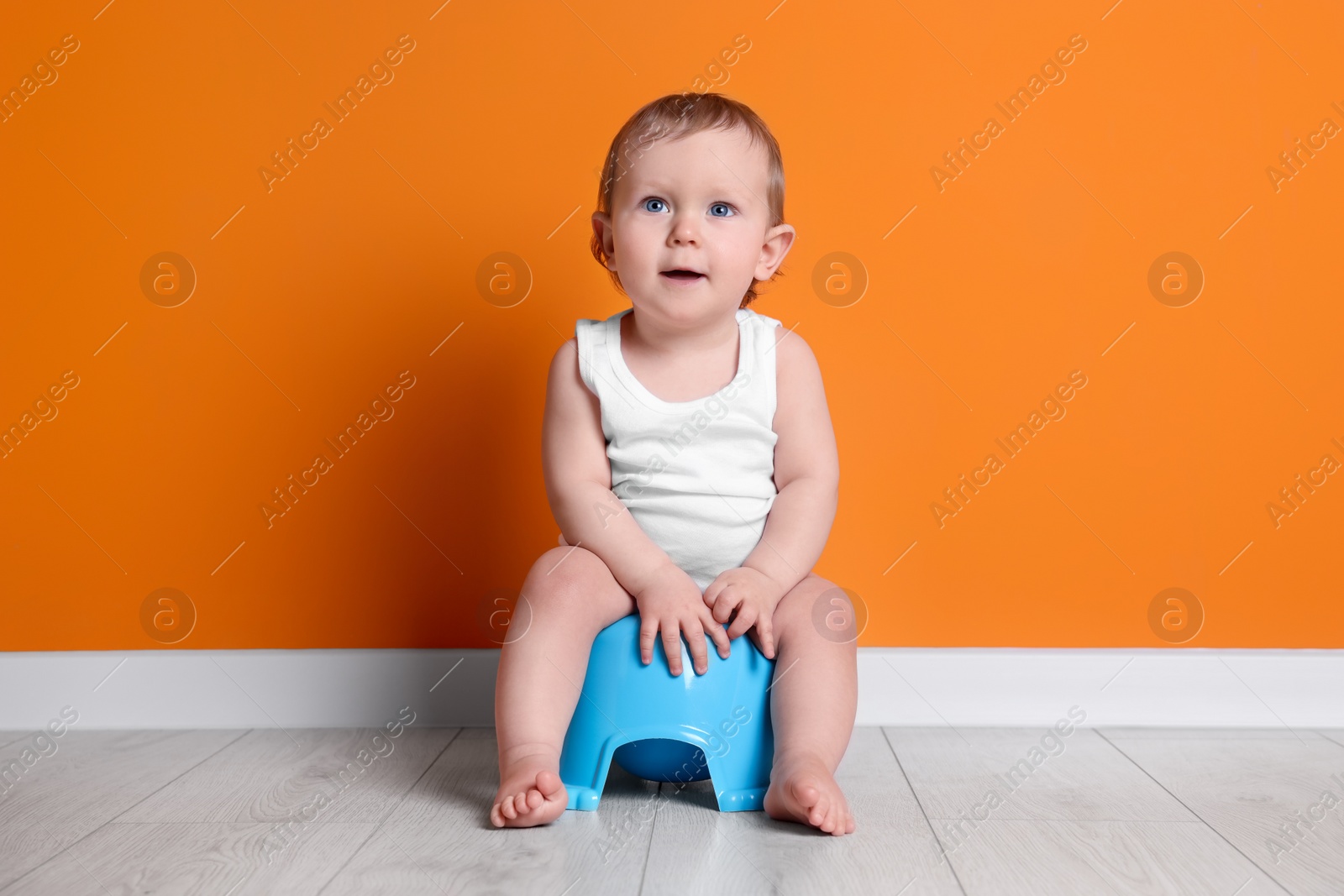 Photo of Little child sitting on baby potty near orange wall