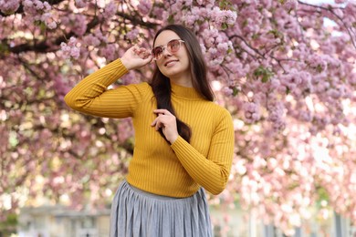 Beautiful woman in sunglasses near blossoming tree on spring day