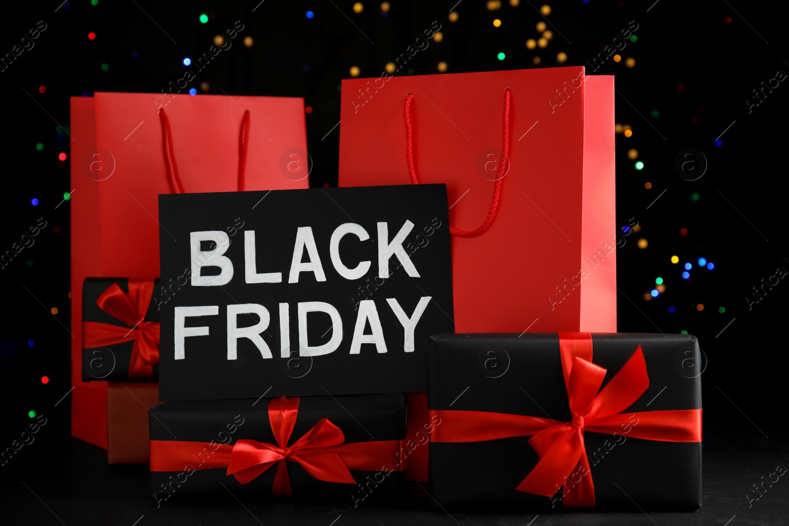 Photo of Paper shopping bags, gift boxes and phrase Black Friday against blurred lights