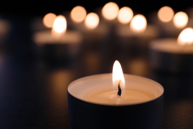 Photo of Burning candle on table in darkness, closeup. Funeral symbol