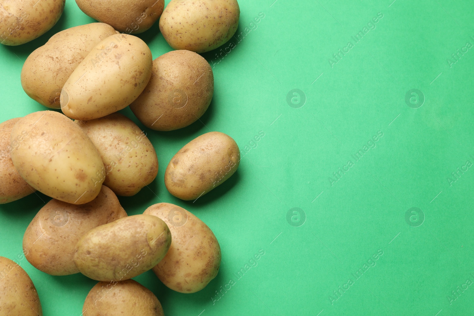 Photo of Fresh raw potatoes on green background, flat lay. Space for text