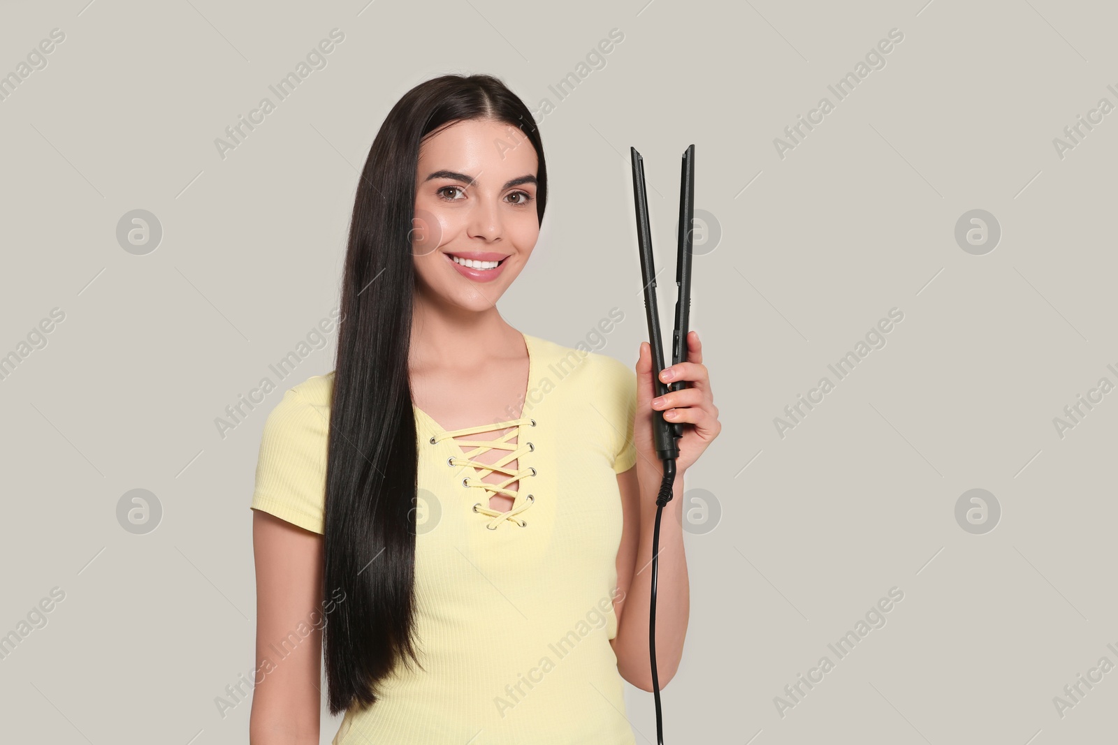 Photo of Beautiful happy woman with hair iron on light grey background. Space for text