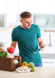 Photo of Man with wooden crate full of products and tablet in kitchen. Food delivery service