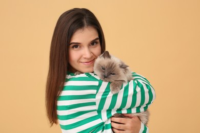 Photo of Woman hugging her cute cat on light brown background