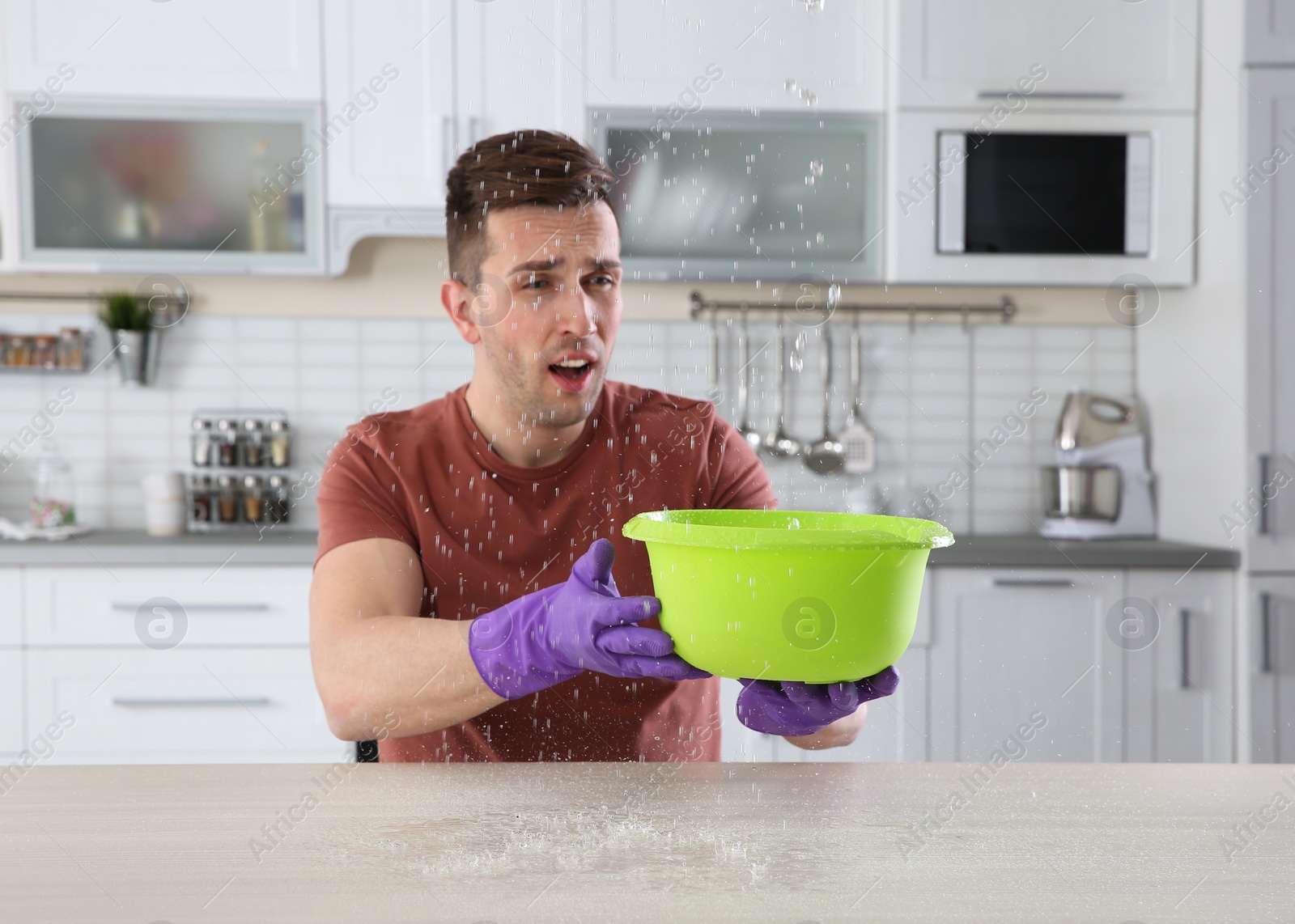 Photo of Emotional man collecting water leaking from ceiling in kitchen. Time to call plumber