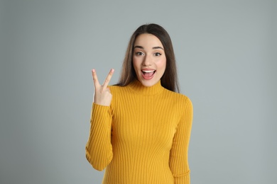 Photo of Woman in yellow turtleneck sweater showing number two with her hand on grey background