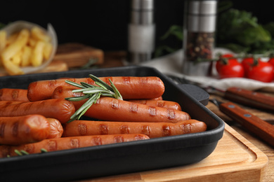 Delicious grilled sausages with rosemary on wooden table, closeup