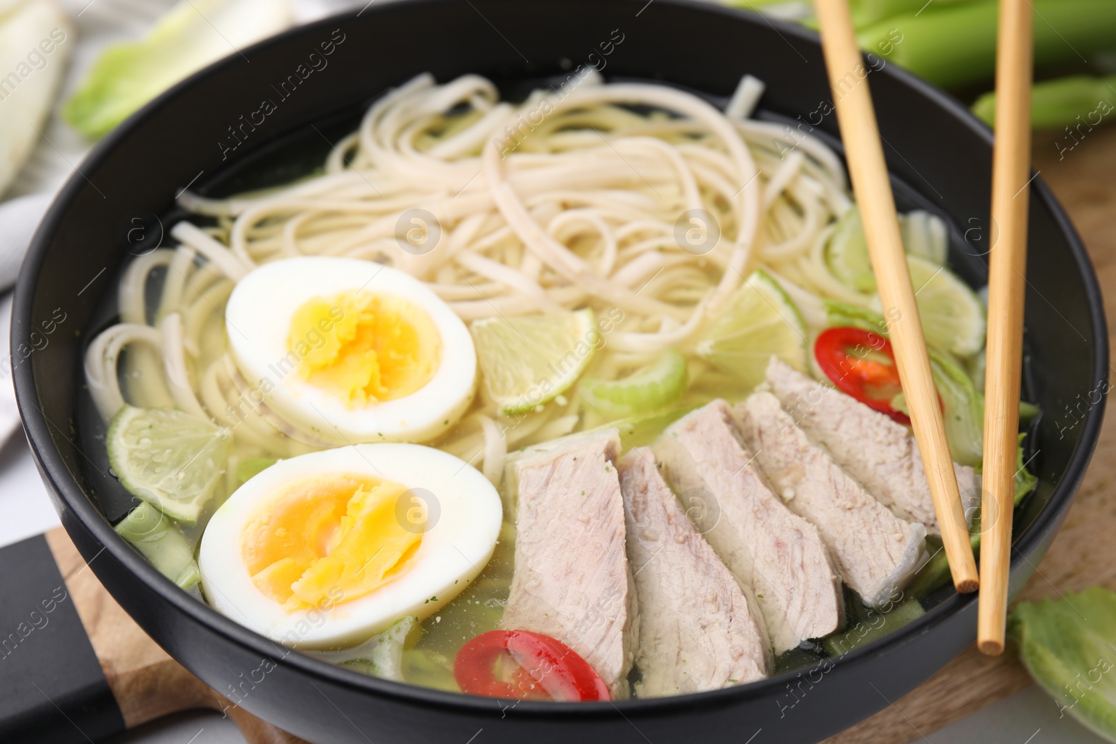 Photo of Bowl of delicious rice noodle soup with meat and egg on wooden board, closeup