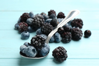 Tasty frozen blackberries and blueberries on light blue wooden table