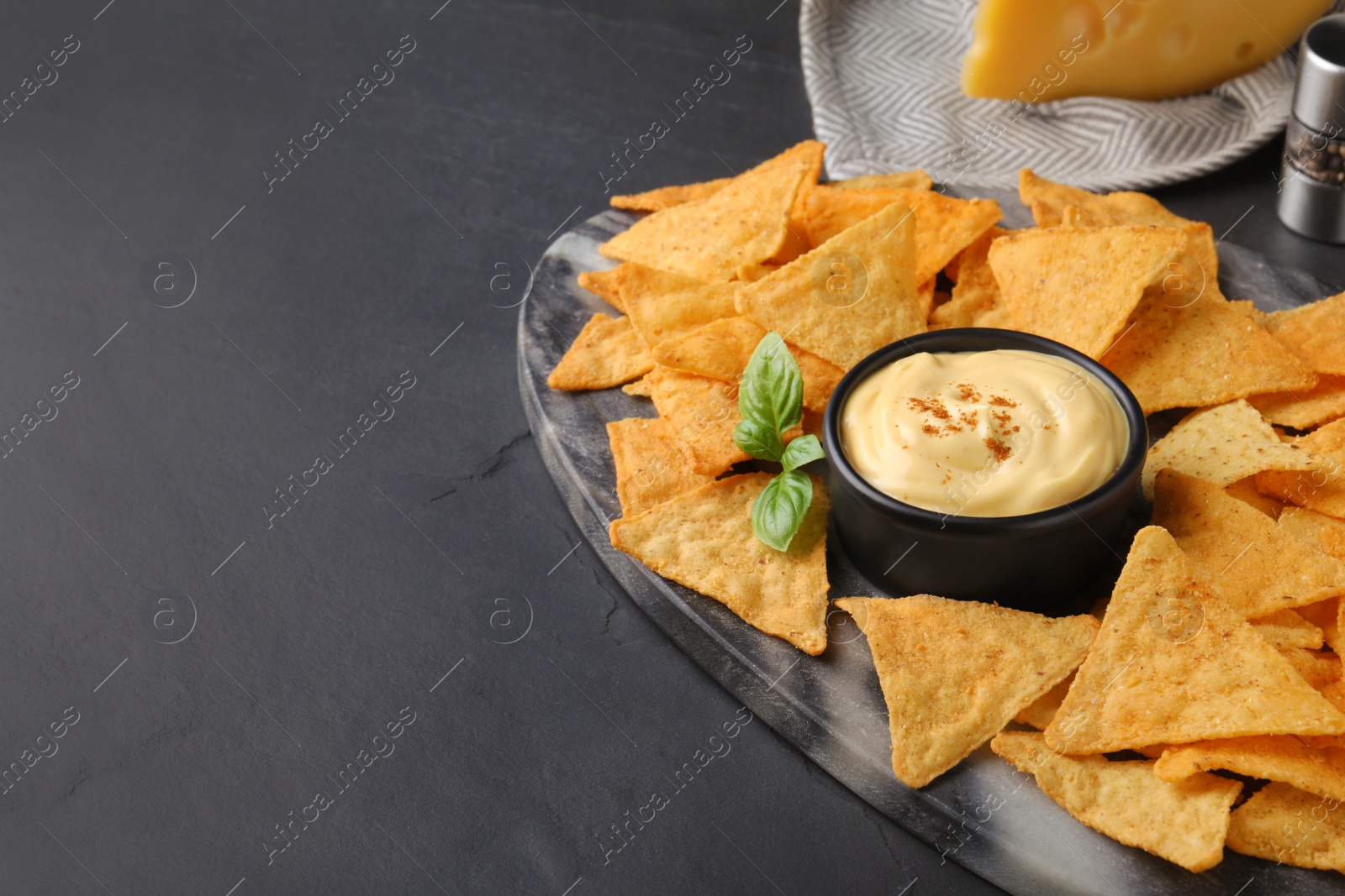 Photo of Delicious nachos and cheese sauce with basil on black table, space for text