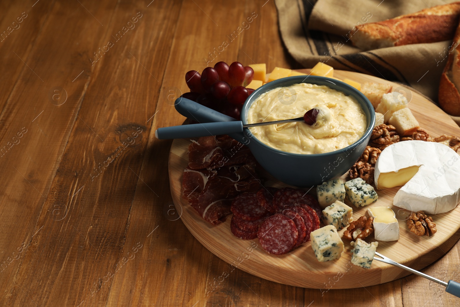 Photo of Fondue pot with tasty melted cheese, forks and different snacks on wooden table