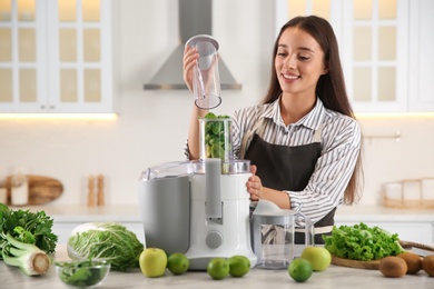 Young woman making tasty fresh juice at table in kitchen