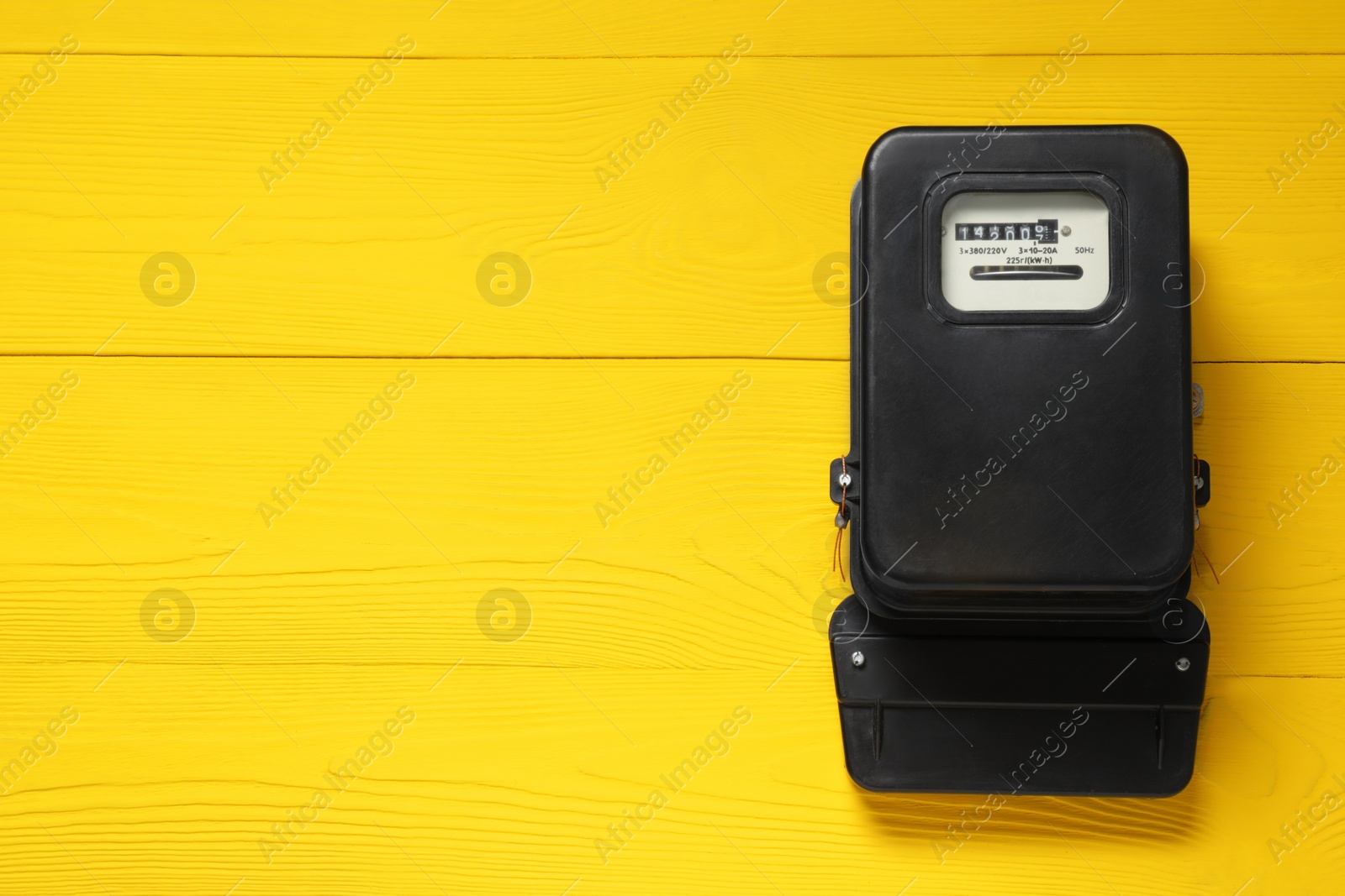 Photo of Electricity meter on yellow wooden wall, space for text