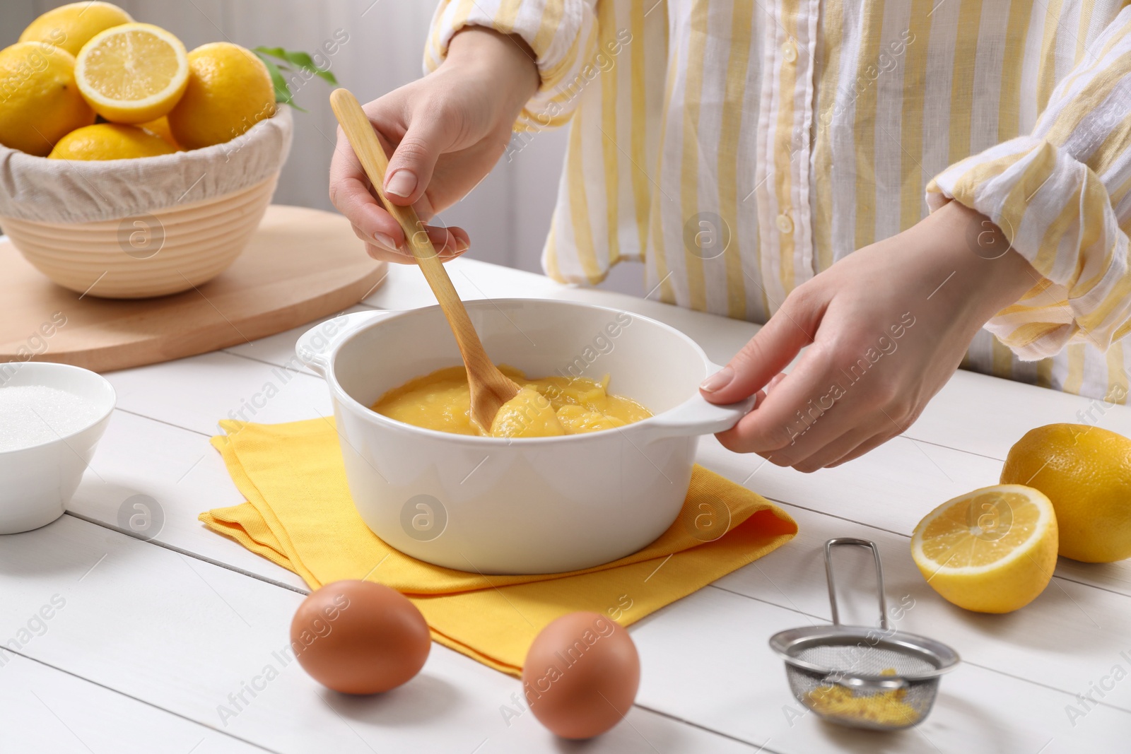 Photo of Woman cooking lemon curd at white wooden table, closeup