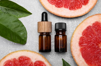 Photo of Bottles of essential oil with grapefruit slices and leaves on grey table, flat lay