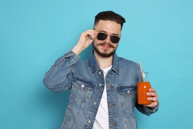 Handsome young man with glass bottle of juice on light blue background