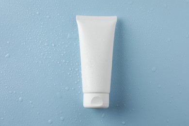 Photo of Moisturizing cream in tube on light blue background with water drops, top view