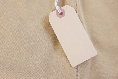 Photo of Cardboard tag on beige garment, top view. Space for text