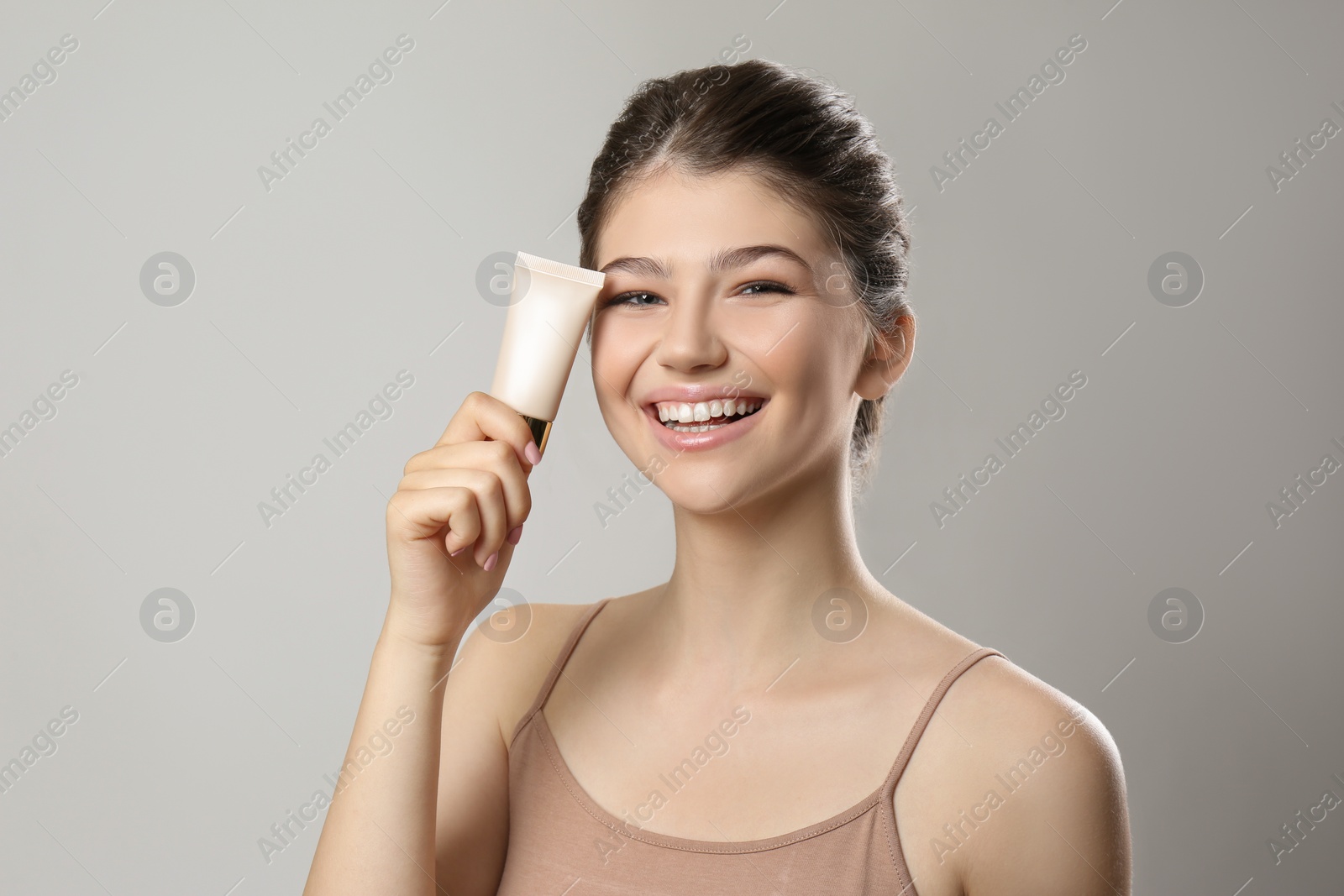 Photo of Beautiful girl with tube of foundation on light grey background