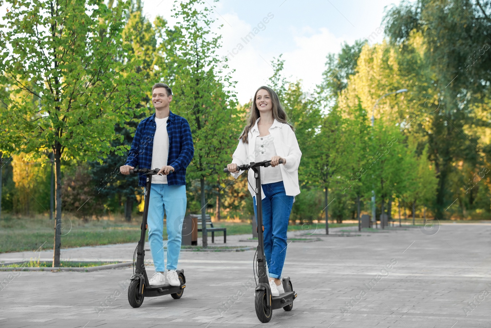 Photo of Happy couple riding modern electric kick scooters in park